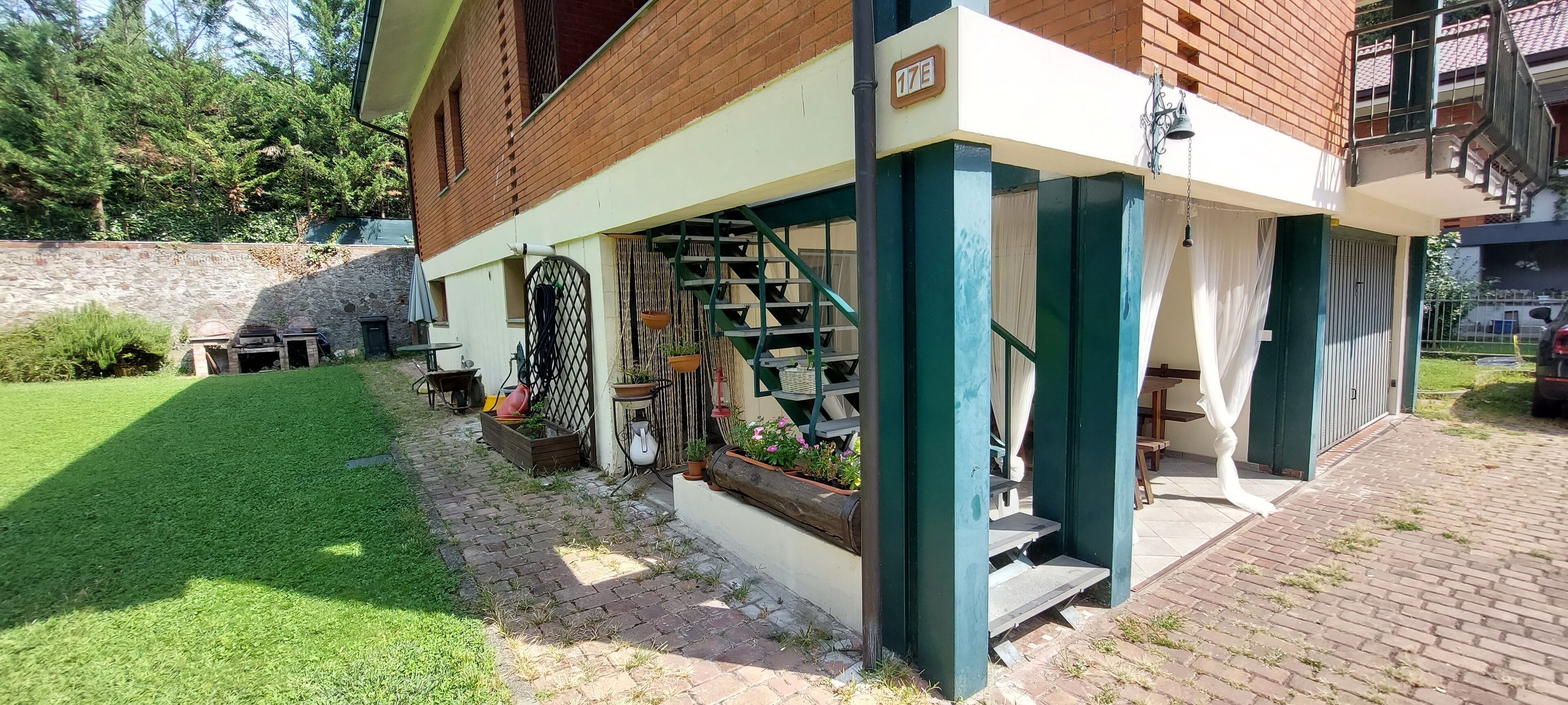 Un edificio residencial con fachada de ladrillo, un área exterior cubierta con una escalera y un pequeño jardín.