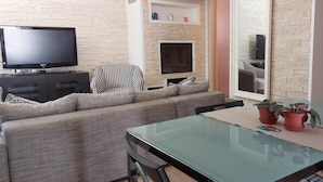 A living room with a sofa, a TV, a fireplace, a dining table with chairs, and a mirror. - A LITTLE NEST (Ivrea)