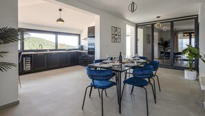 A modern kitchen with dark cabinetry, a large window, and a dining area with blue chairs and a table set for a meal.