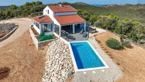 A villa with a swimming pool, outdoor seating, and a view of the surrounding landscape.