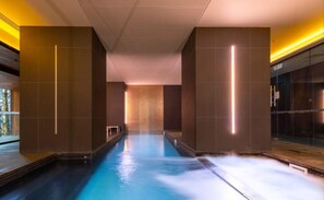 A modern indoor swimming pool with a clear view of the pool's length, surrounded by dark walls and a bright ceiling.