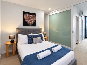 Une chambre moderne avec un lit, deux lampes de chevet, une œuvre d’art en forme de cœur, une porte coulissante et une vue sur l’extérieur.