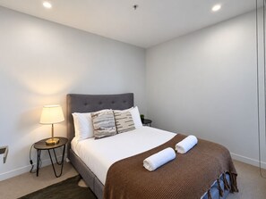 Una camera da letto moderna con un letto, un comodino con una lampada e una coperta marrone.