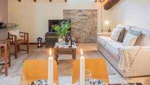 A cozy living room with a wooden ceiling, a stone wall, a sofa, a TV, and a dining table with candles. - Plinio 10 in Como With 2 Bedrooms and 2 Bathrooms (Como)