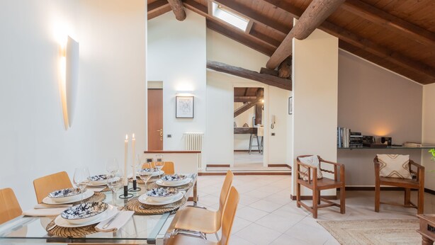 A dining area with a glass table set for six, wooden chairs, and a view of the kitchen through an open doorway. - Plinio 10 in Como With 2 Bedrooms and 2 Bathrooms (Como)