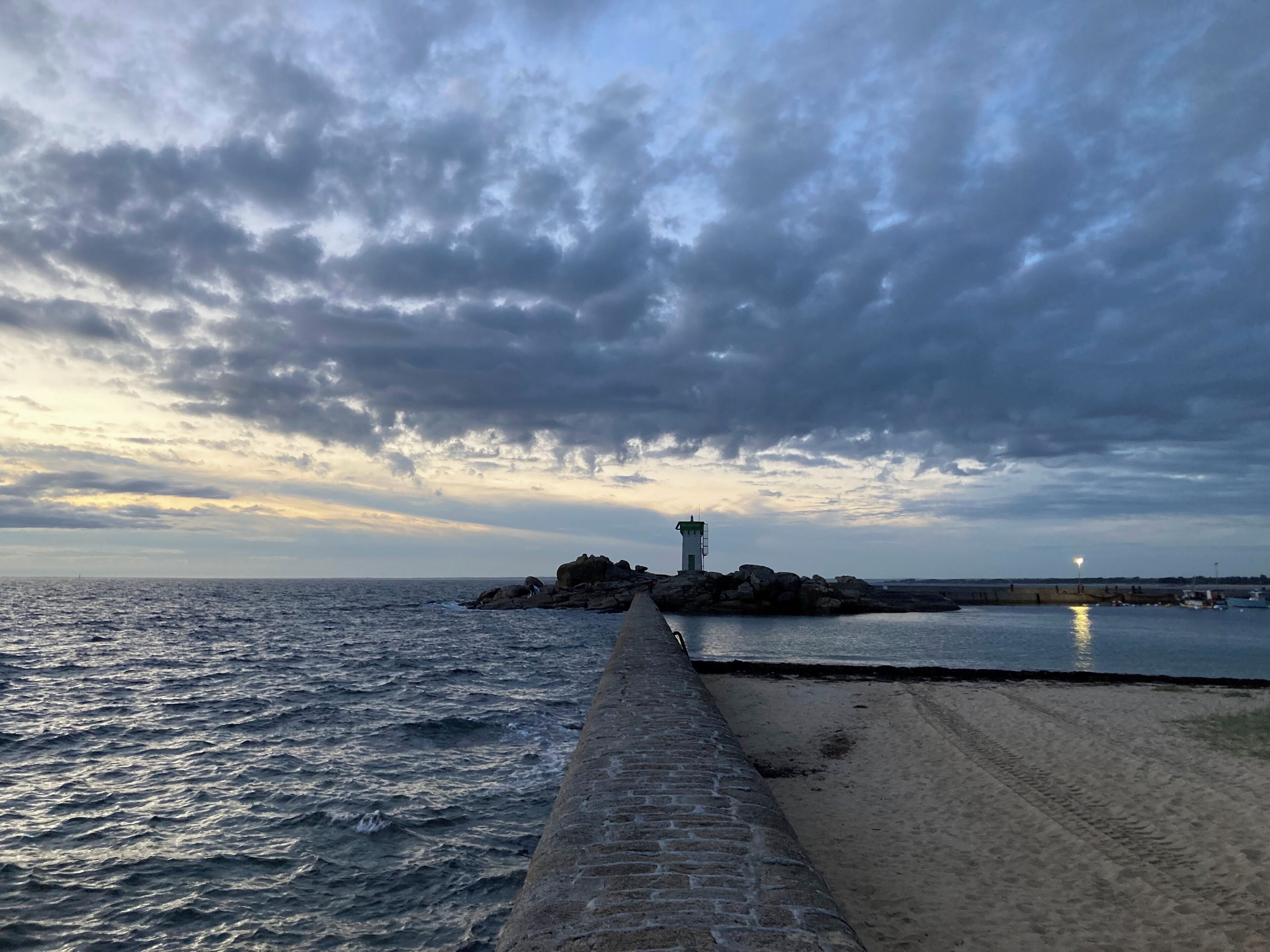 Un paisaje costero con un promontorio rocoso, un faro y una playa arenosa.
