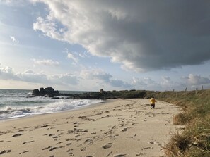 A sandy beach with footprints leading towards the water, a rocky outcrop, and a grassy dune area. - Terre et mer Bretagne (Trégunc)