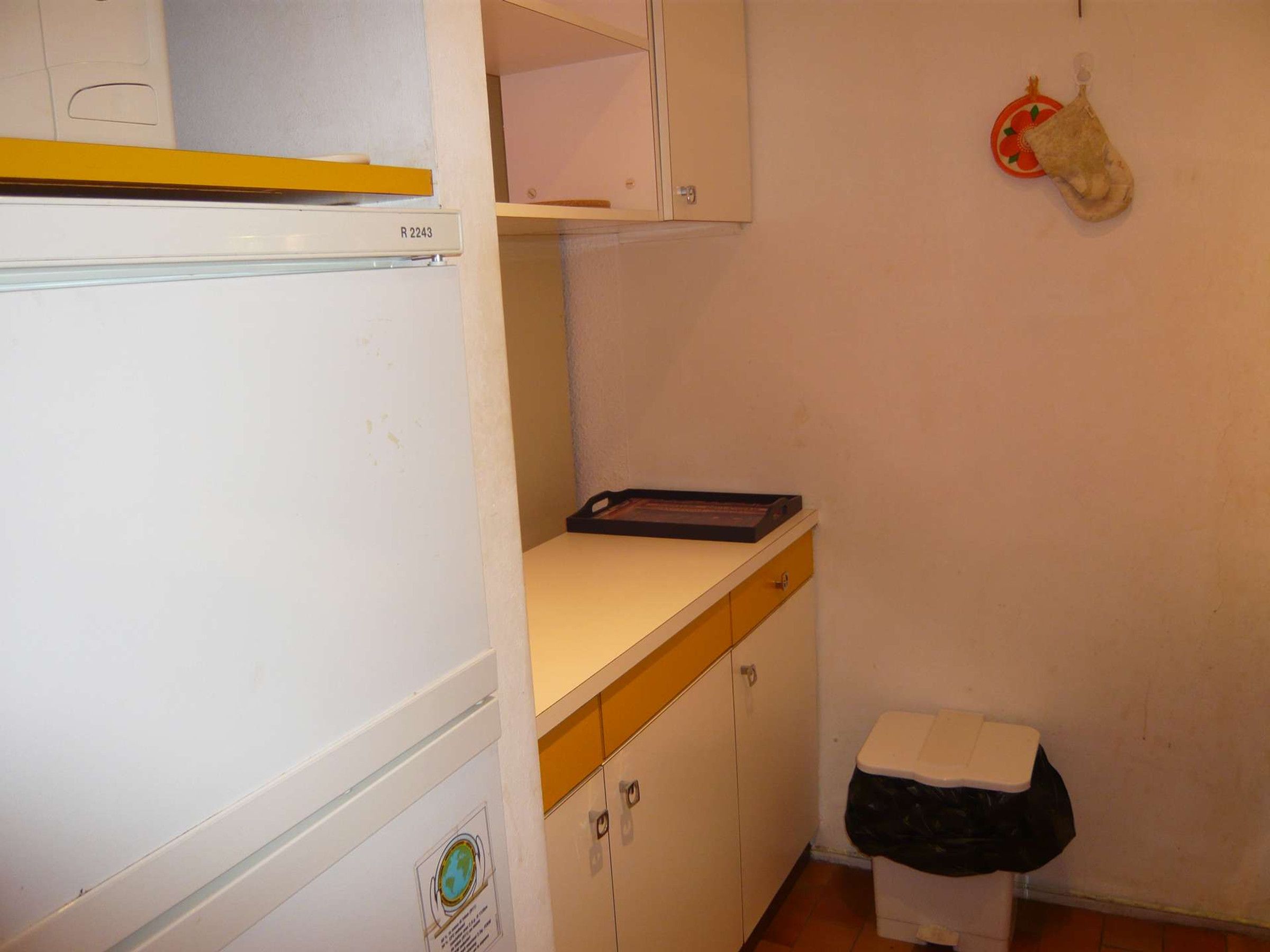 Eine kleine Küche mit Kühlschrank, Arbeitsfläche und einem Wäschekorb.