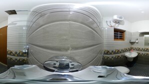 A bathroom with a large, curved mirror, a toilet, a sink, and a shower area. - Zavon Holiday Home -Deluxe Room (Vythiri)