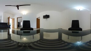 A room with a glass table, two black chairs, a ceiling fan, and a mounted television. - Zavon Holiday Home -Deluxe Room (Vythiri)