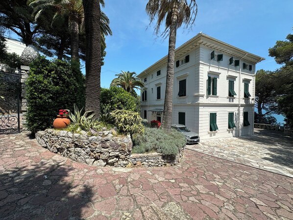 A two-story building with a stone facade, green shutters, and a paved courtyard.