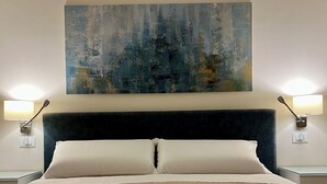 A neatly made bed with a textured beige blanket, a dark headboard, and a large abstract painting above it. - Novimo Comfort Apartment with elevator and secure private parking (Terrasini)