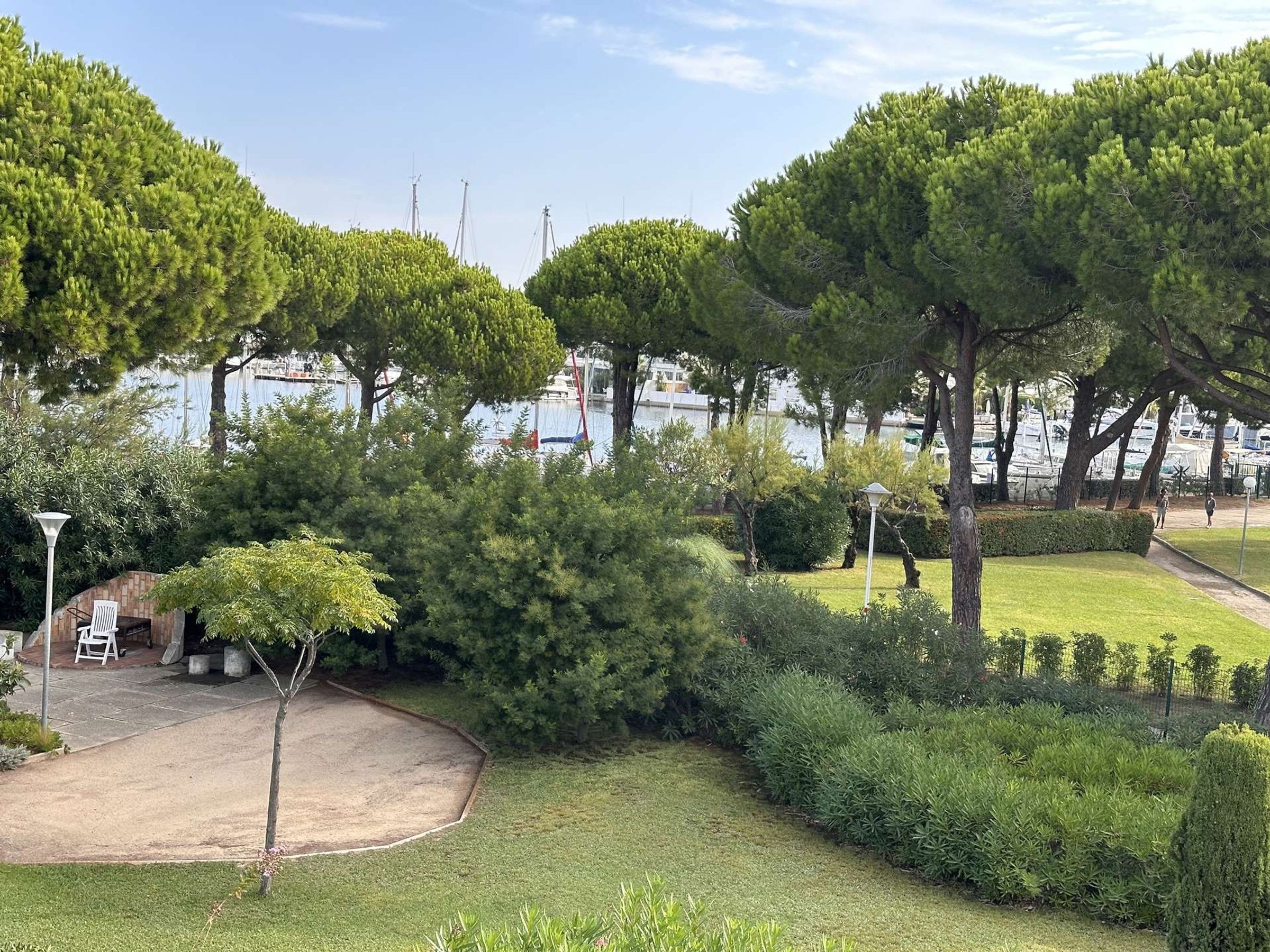 A landscaped garden with trees, a paved area, and a view of boats on water.