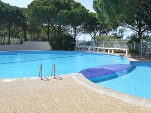 A swimming pool with a pebble-lined edge, surrounded by trees and a fence.