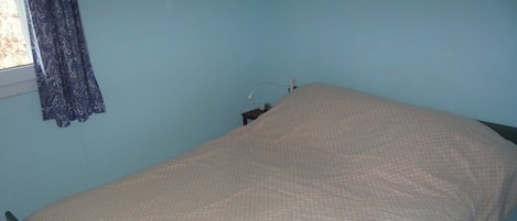 Una cama individual con una colcha estampada en una habitación con paredes azul claro y una ventana con cortinas decoradas.