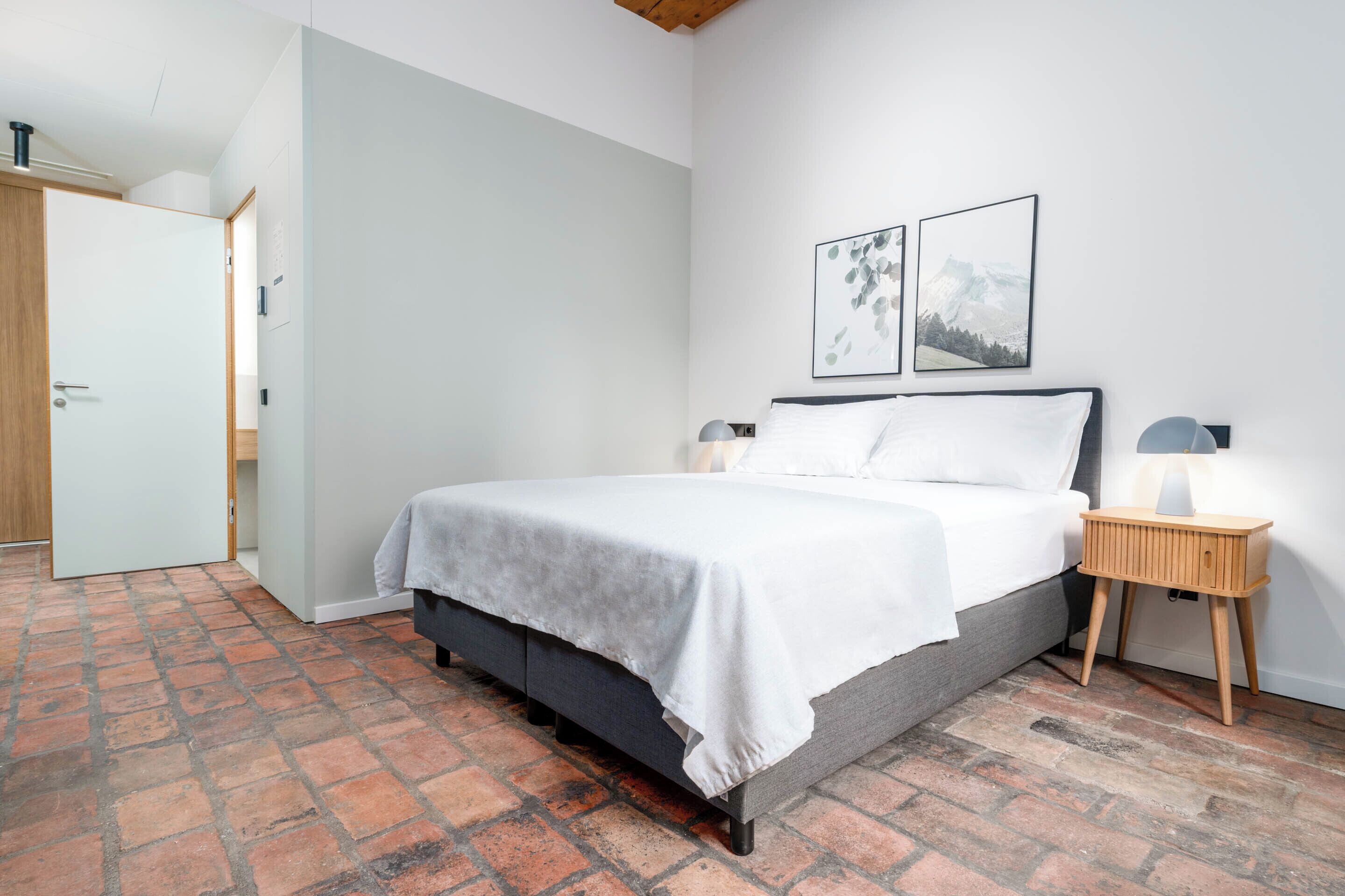 Een slaapkamer met een bed, nachtkastjes en een vloer met een baksteenmotief.