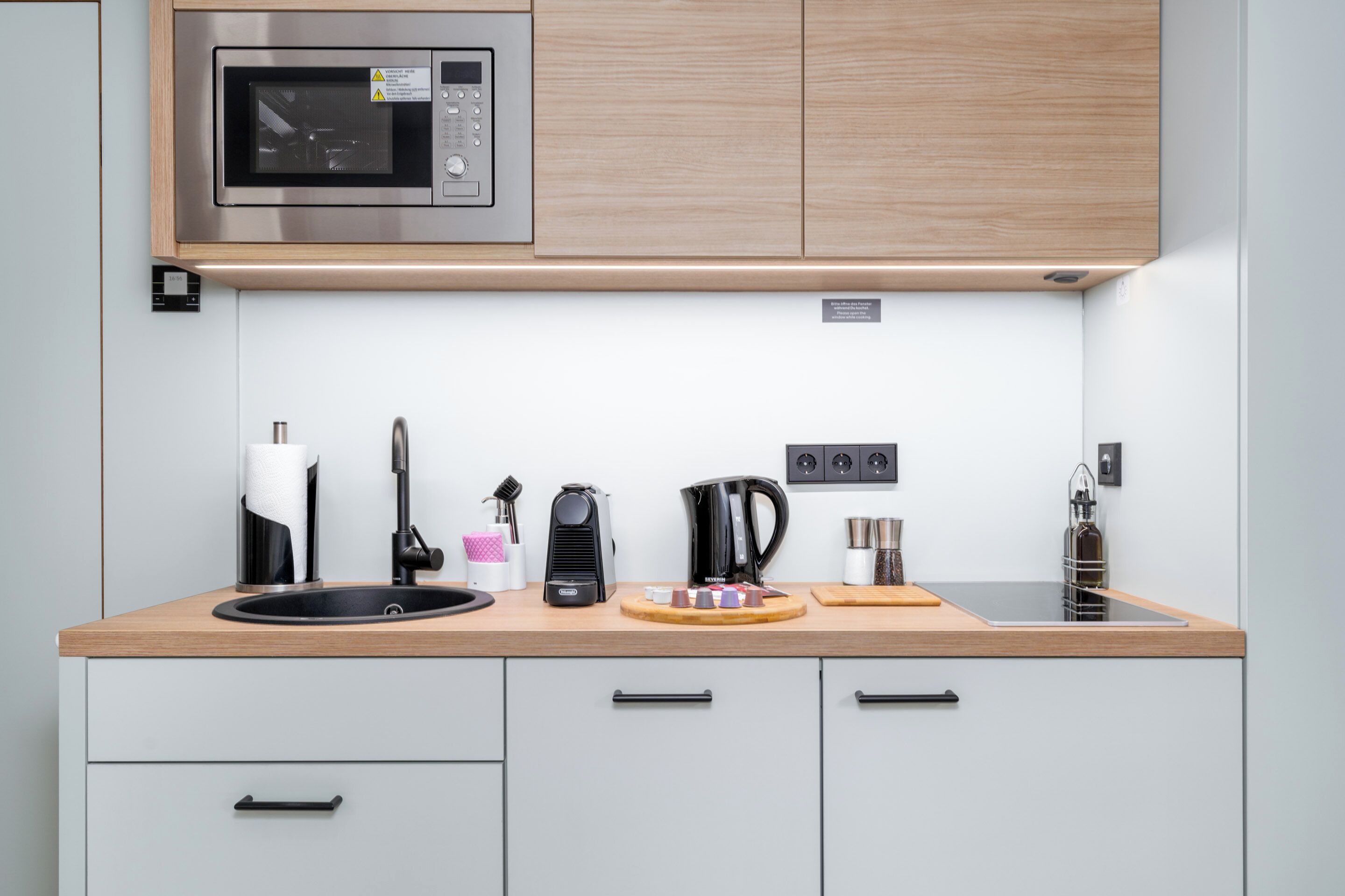 A modern kitchen with a built-in microwave, a coffee maker, a kettle, and a sink.