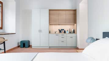 A bedroom with a wooden ceiling, a bed, a nightstand, a wardrobe, and a kitchenette area.