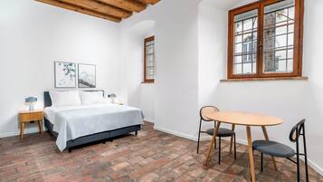 Une chambre à coucher avec un lit, une petite table et deux chaises, une fenêtre avec des cadres en bois et un plancher en briques.