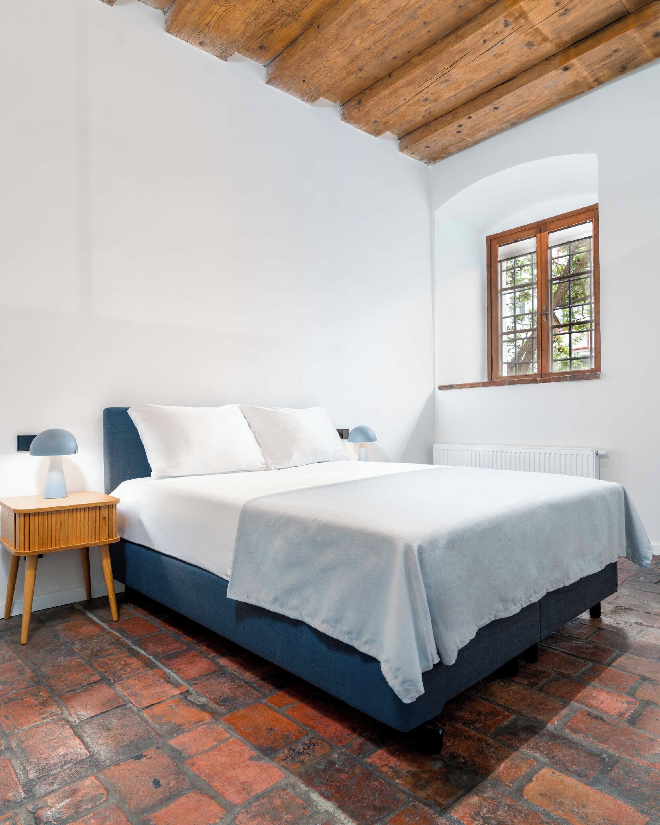 Ein Schlafzimmer mit Bett, Nachttisch, Fenster und Heizkörper.