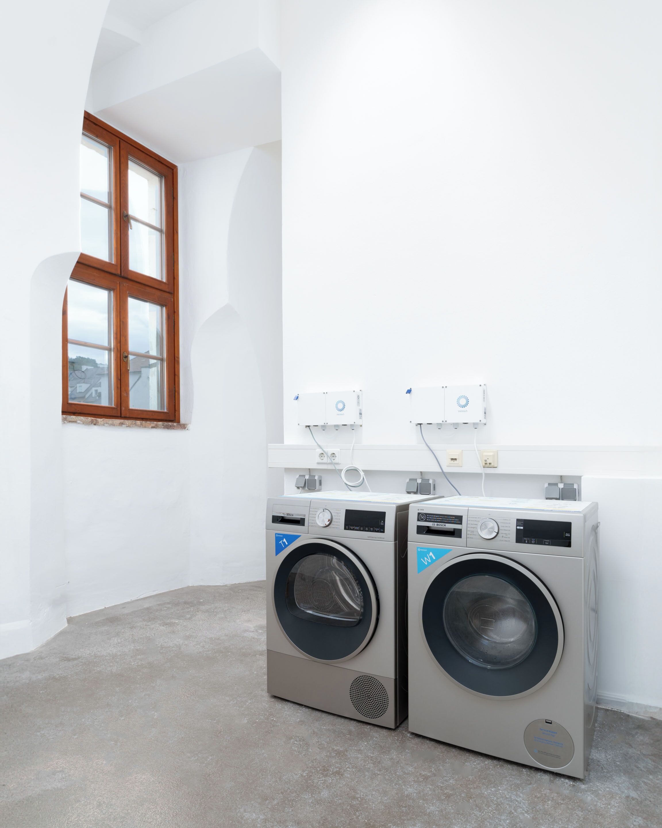 A laundry room with two front-loading washing machines, a window, and a white wall.