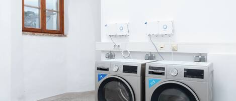 A laundry room with two front-loading washing machines, a window, and a white wall.