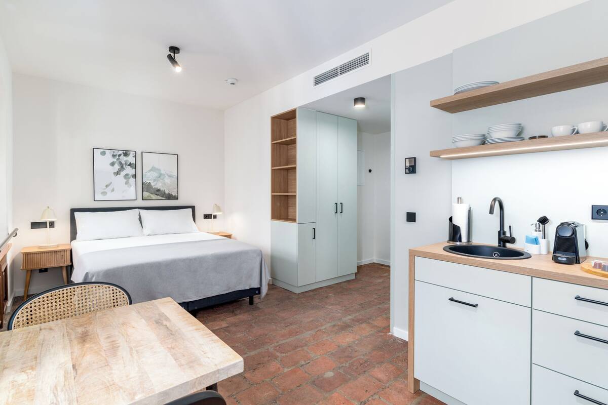 Een compacte hotelkamer met een bed, een klein tafeltje, een kitchenette en een badkamer.