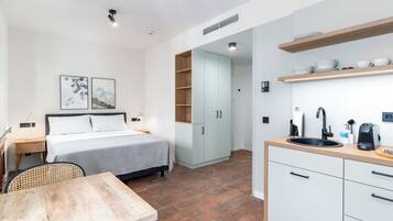 Ein kompaktes Hotelzimmer mit Bett, kleinem Tisch, Küchenzeile und Bad.