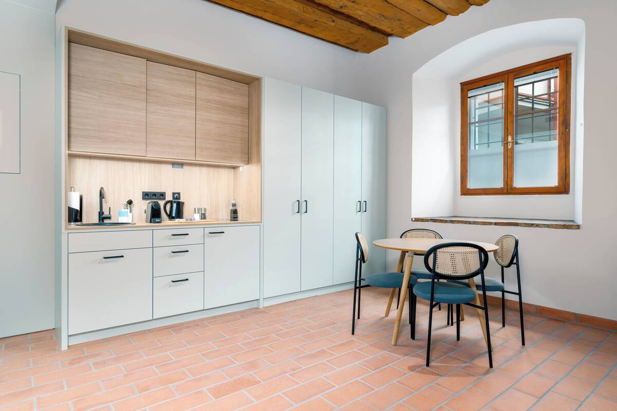 Een keuken met witte kasten, een houten plafond en een eethoek met een tafel en stoelen.