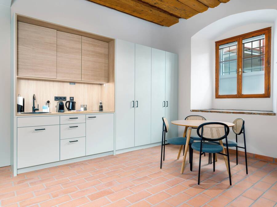 Una cocina con armarios blancos, techo de madera y una zona de comedor con una mesa y sillas.