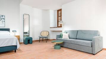 Una habitación de hotel moderna con una cama, un sofá gris, una mesita redonda pequeña, una silla y un espejo grande.