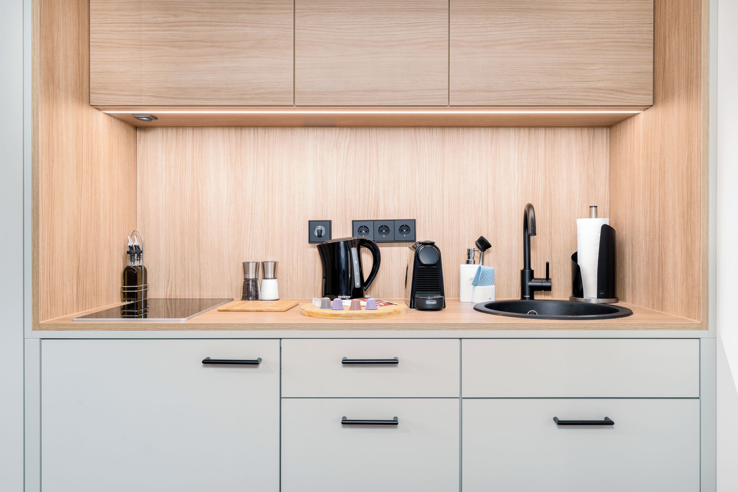 A modern kitchen with wooden cabinets, a black kettle, a coffee maker, and a sink.