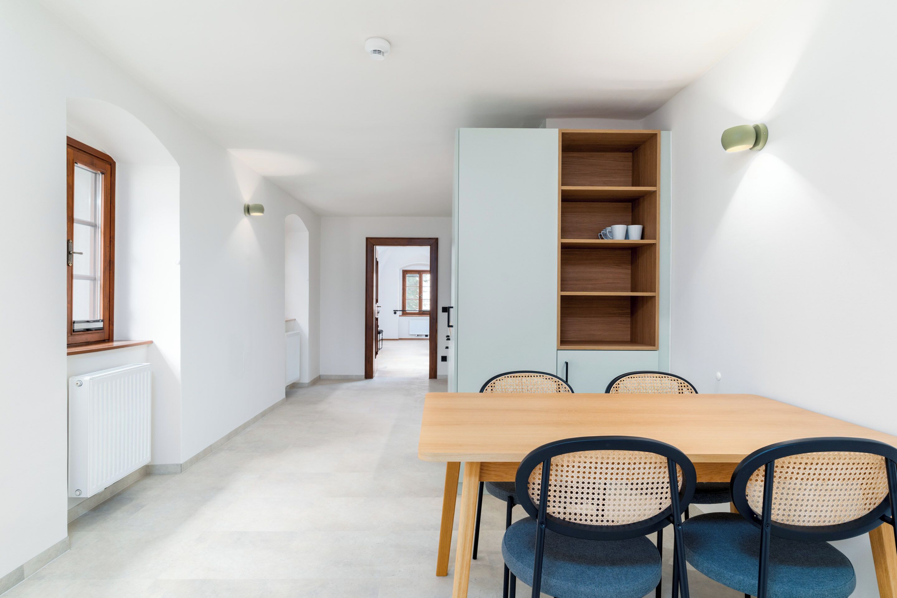 Un comedor con una mesa de madera y cuatro sillas, un armario azul claro con estantes, y un radiador blanco en la pared.