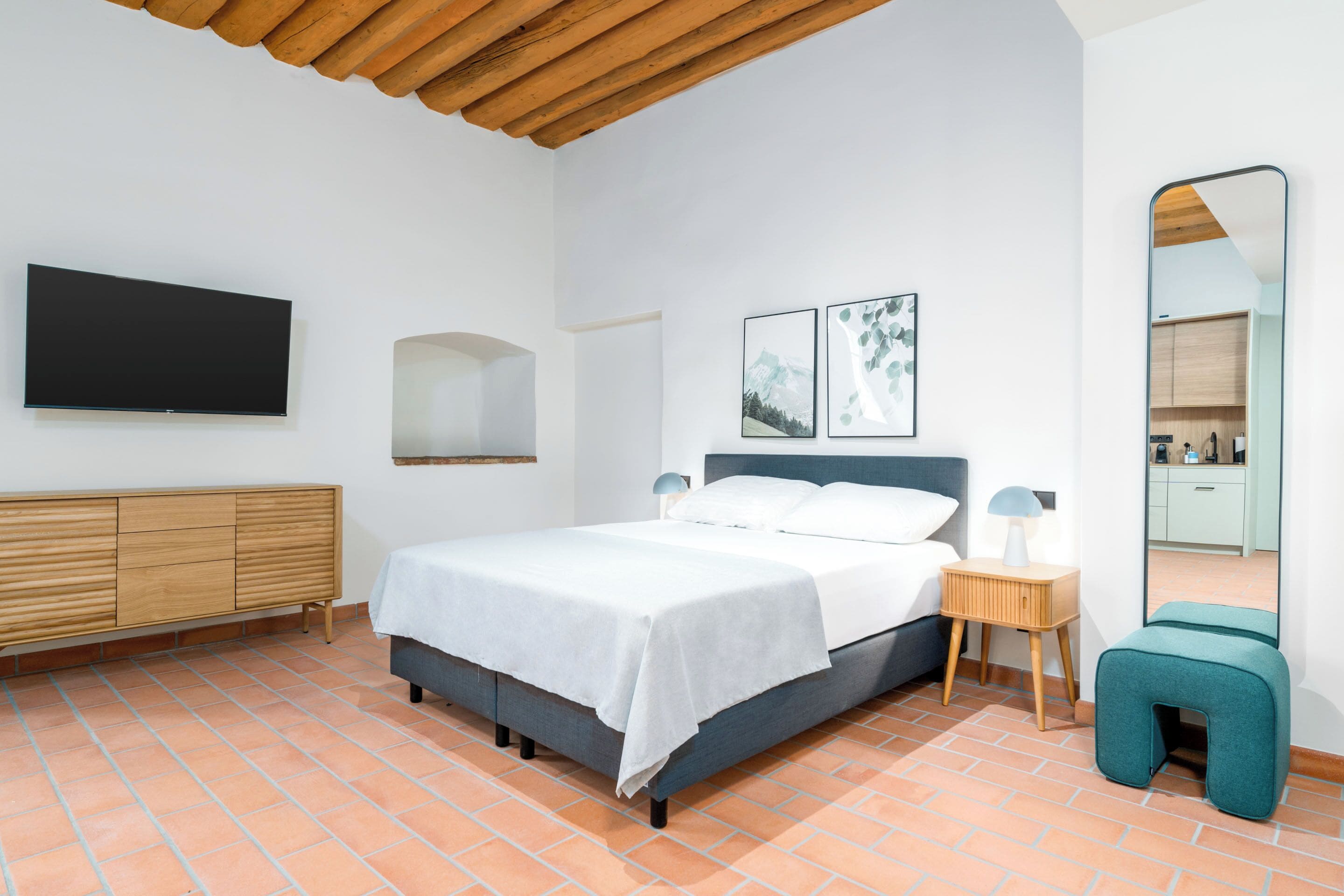 A bedroom with a bed, a nightstand, a mirror, and a wall-mounted TV.