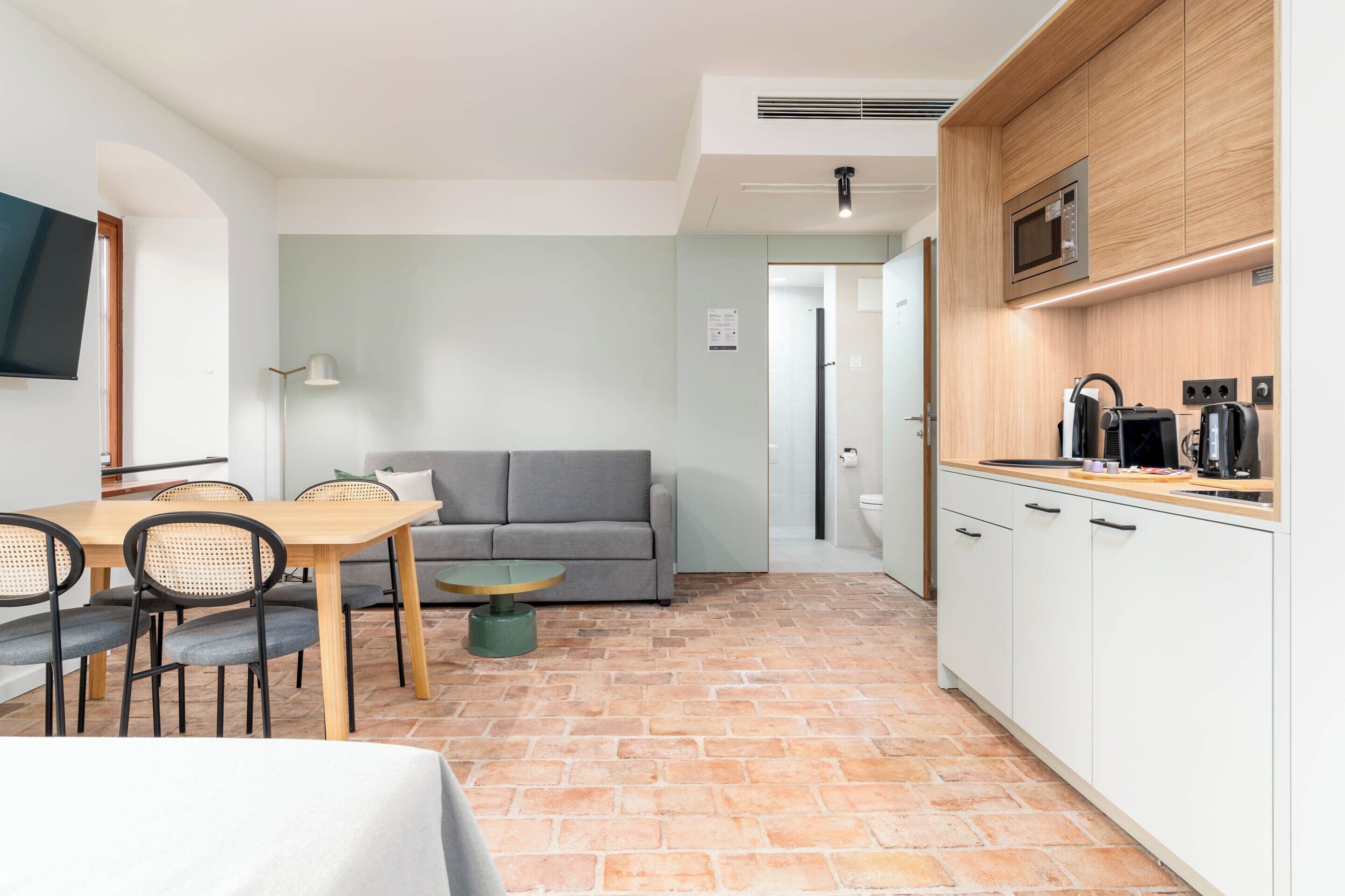 A compact living space with a dining area, a sofa, a kitchenette, and a TV mounted on the wall.