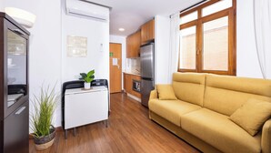 A compact living space with a kitchenette, a sofa, a small table with a plant, and a potted plant by the sofa. - Apartamentos Turísticos Distrito Romano (Cartagena)