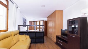A modern living room with a sofa, wooden cabinets, a TV, and a glass cabinet with cups and a wine glass. - Apartamentos Turísticos Distrito Romano (Cartagena)