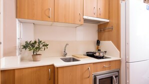 A kitchen with wooden cabinets, a white countertop, a sink, a stove, and a microwave. - Apartamentos Turísticos Distrito Romano (Cartagena)