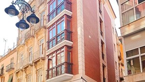 A multi-story building with a red brick facade, multiple balconies, and a corner entrance. - Apartamentos Turísticos Distrito Romano (Cartagena)