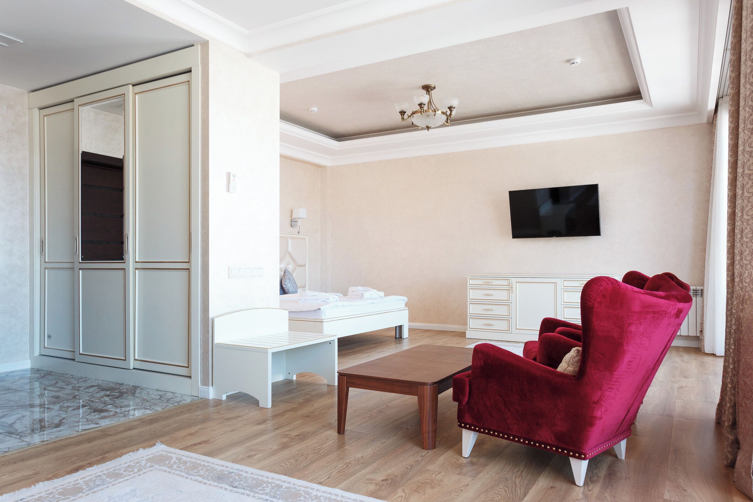 A modern living room with a wooden floor, a white desk, a red armchair, and a TV mounted on the wall.