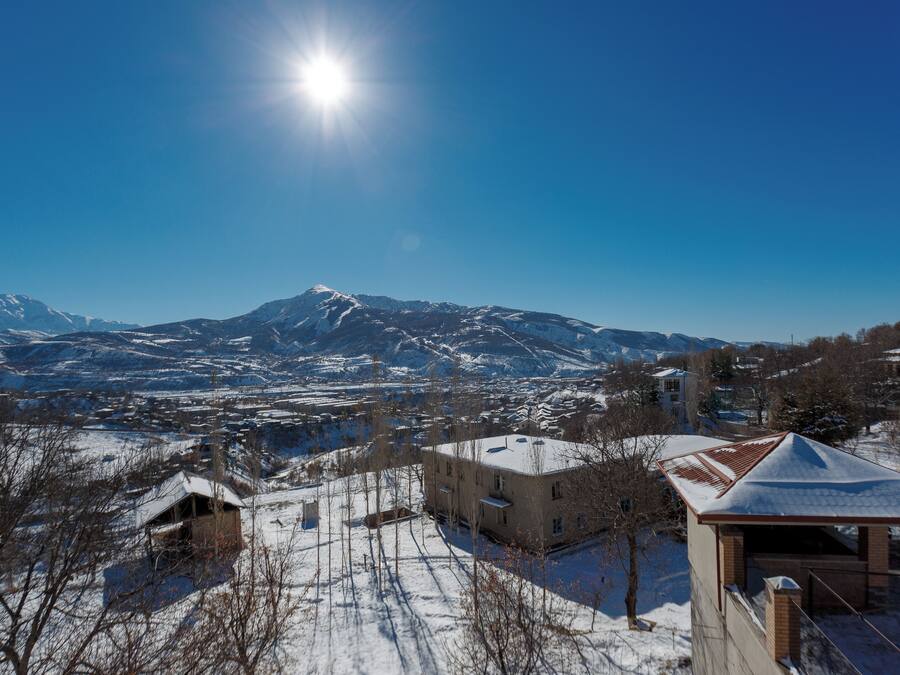 A snow-covered landscape with a mountain in the background and a building with a snow-covered roof in the foreground.