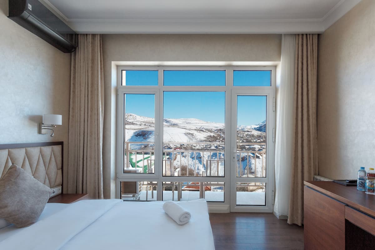 A hotel room with a large window, a bed, a desk, and a view of a snowy landscape.