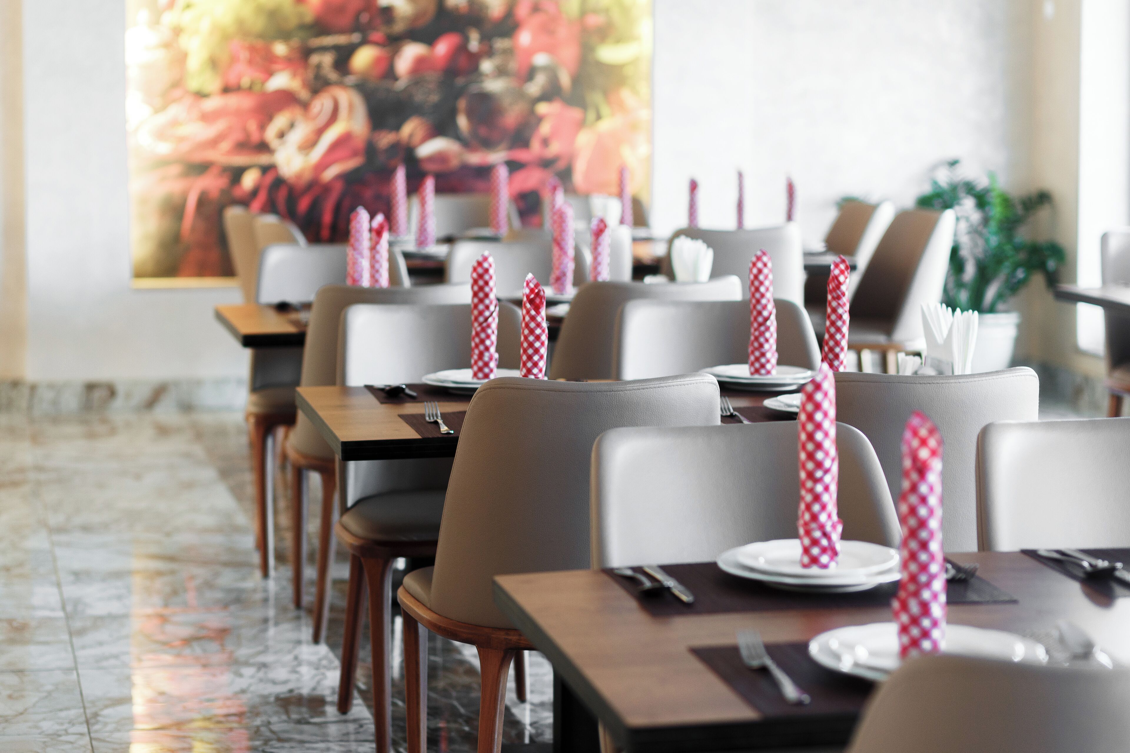 A restaurant with tables set with white plates, red and white checkered napkins, and wooden chairs.