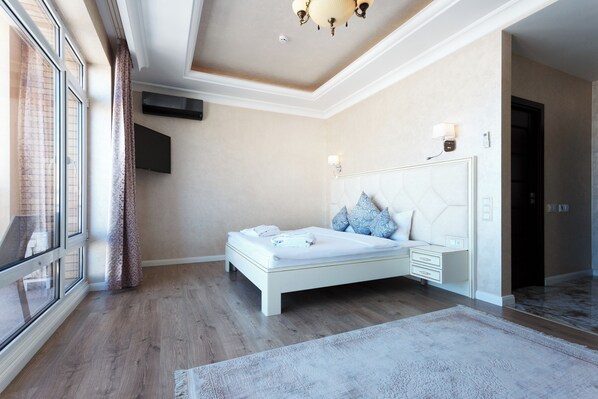 A modern bedroom with a large bed, a flat-screen TV, and a view of the city through large windows. - Panoramic SPA Hotel (Chorvoq)