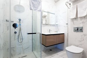 Ett modernt badrum med en dusch som är avskärmad med glasväggar, ett vitt handfat och en toalett.