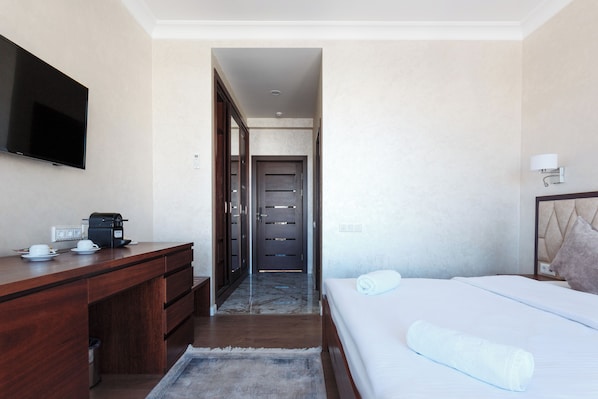 A hotel room with a bed, a desk with a coffee maker, a TV, and a door leading to another room. - Panoramic SPA Hotel (Chorvoq)