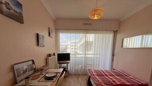 A small, well-lit room with a bed, a TV, a dining table, and a window with sheer curtains. - Central Arcachon Apartment: Beach & Shops on Foot (Arcachon)