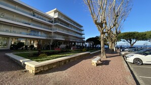 A multi-story hotel with balconies, a landscaped garden, and a parking area with cars. - Central Arcachon Apartment: Beach & Shops on Foot (Arcachon)