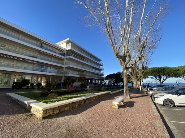 A multi-story hotel with balconies, a landscaped garden, and a parking area with cars.