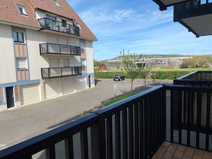 Ein Wohngebäude mit Balkon, Parkplätzen und Blick auf einen Park sowie weitere Gebäude in der Ferne.
